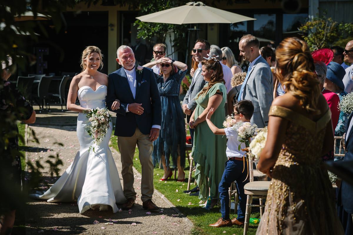 father walks bride down the isle of her outdoor country house wedding surrey same_sex_wedding gay_couple natural authentic documentary wedding photo photographer