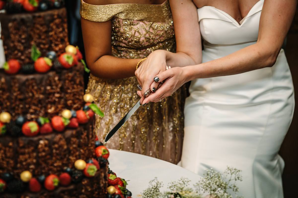 cutting of the wedding cake at lesbian wedding in lgbtq friendly outdoor wedding venue russets country house surrey for same_sex_wedding and natural authentic wedding portraits by documentary wedding photographer