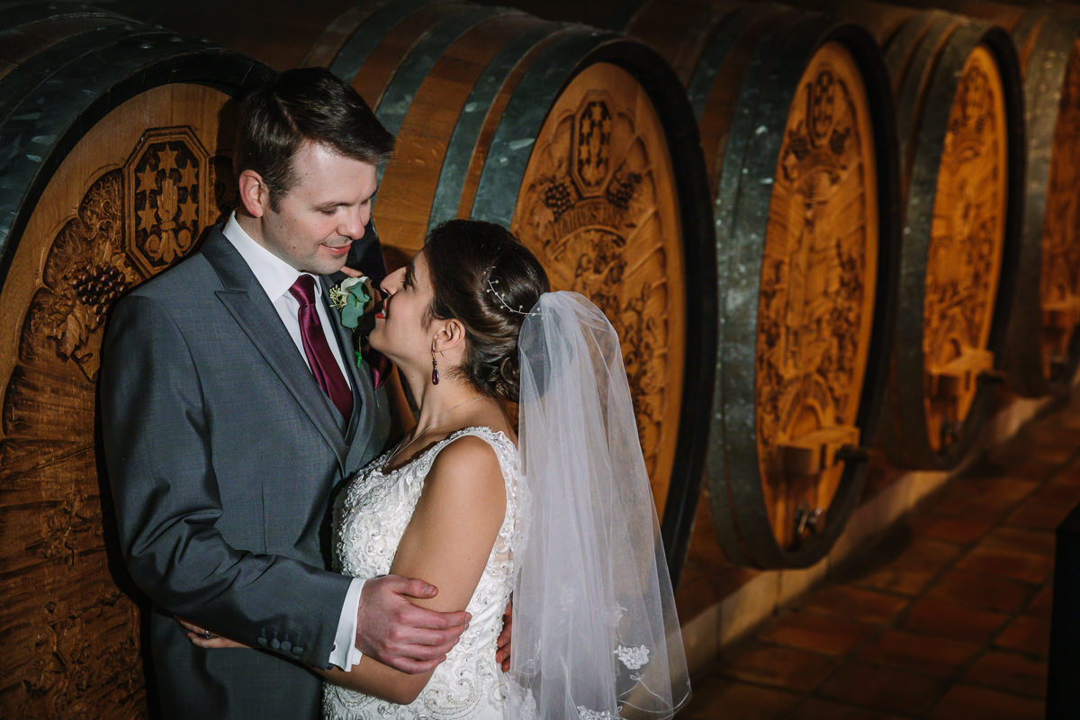 off_camera_flash bride groom indoor wedding portrait in front of wooden barrels in wine cellar at denbies vineyard dorking by documentary wedding photographer surrey for natural colourful and authentic wedding photography