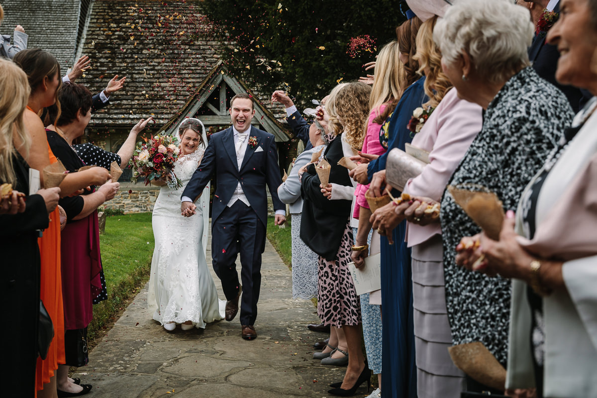 bride and groom wedding confetti exit at st_peter church newdigate natural colourful authentic wedding photography by documentary wedding photographer guildford surrey and horsham west_sussex