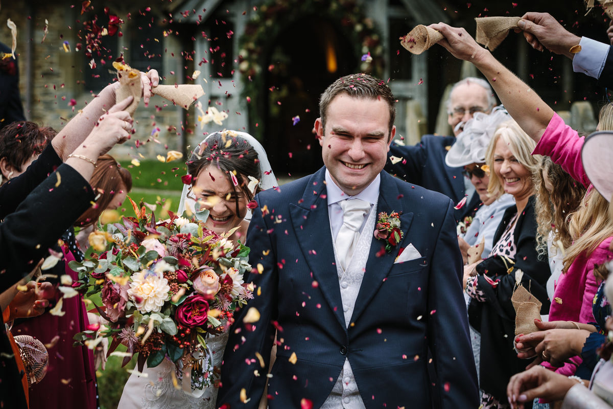 bride and groom wedding confetti exit at st_peter church newdigate natural colourful authentic wedding photography by documentary wedding photographer guildford surrey and horsham west_sussex
