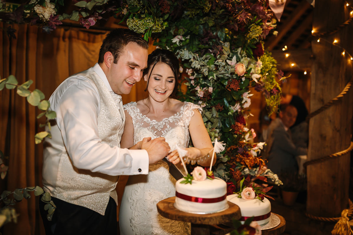 gildings barns newdigate bride and groom wedding cake cutting natural authentic colourful wedding portraits by documentary wedding photographer guildford surrey and horsham west_sussex