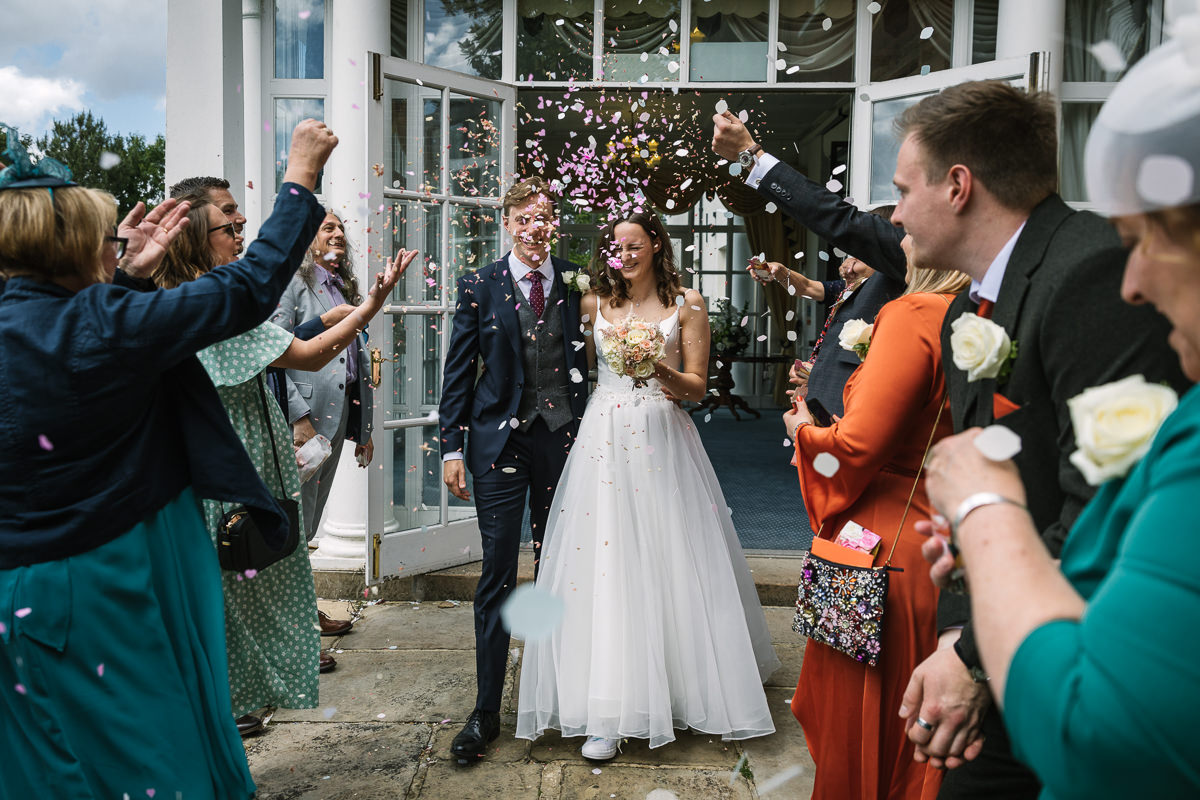 Bride and groom kiss confetti exit after wedding ceremony registry_office Leatherhead by lgbtq_friendly documentary wedding photographer surrey Sussex for natural candid colourful authentic unposed relaxed wedding photography
