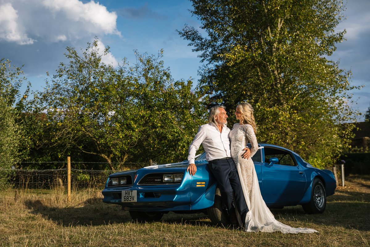 bride and groom portrait with wedding car transam trans am at outdoor tipi wedding dorking surrey by documentary wedding photographer sussex for candid natural unposed authentic LGBTQ_friendly documentary photography