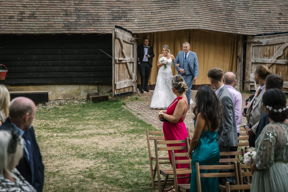 bride arriving with father at outdoor wedding ceremony gildings barns surrey unposed natural candid documentary photography sussex