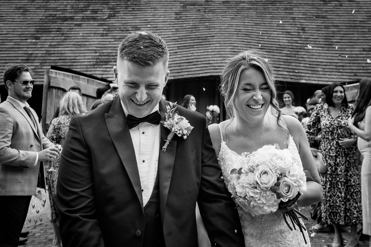 black_and_white image of bride and groom in confetti walk just after wedding ceremony at gildings barns surrey unposed natural candid documentary photography sussex
