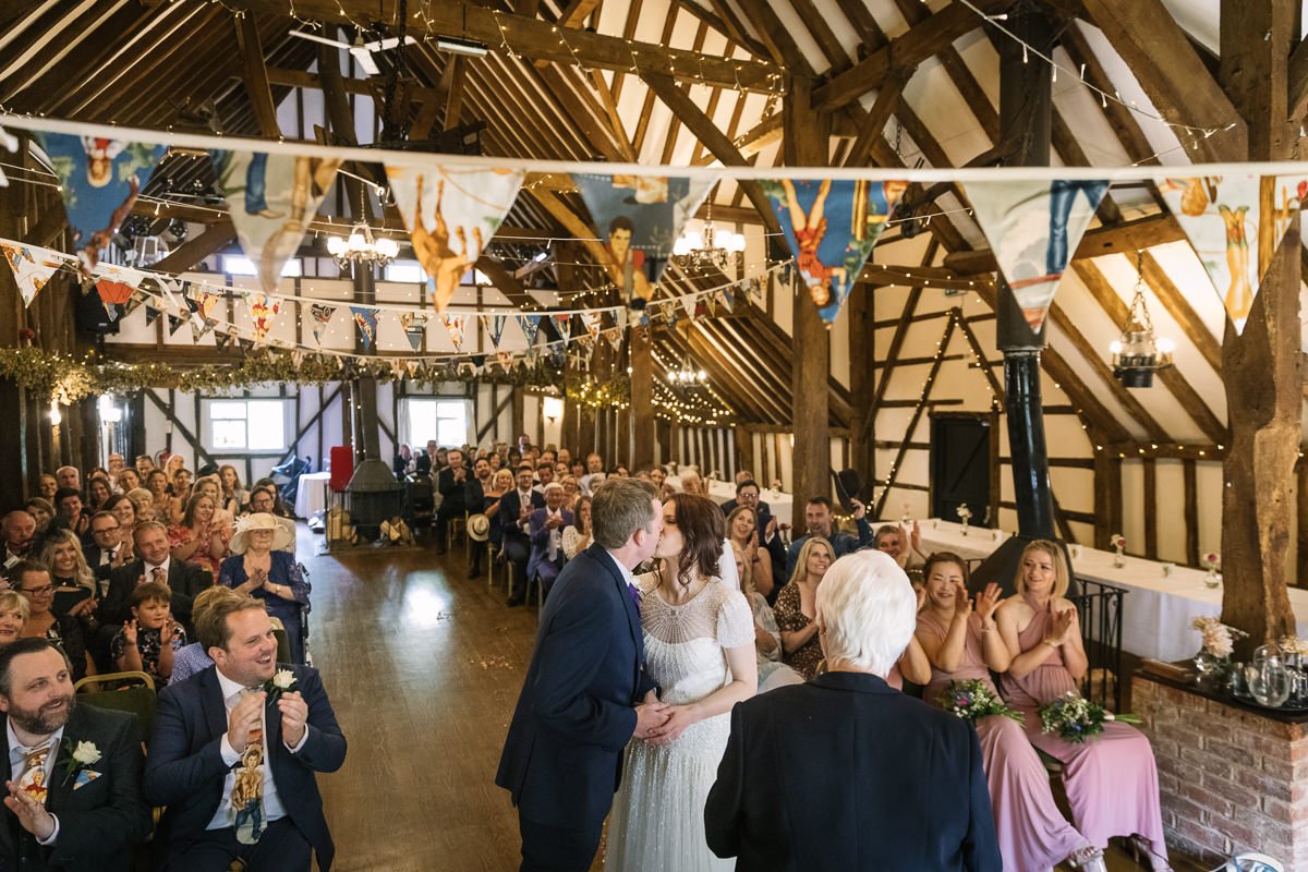 bride and groom kiss during wedding ceremony in barn at barn wedding venue kent the_plough_at_leigh bride and groom natural authentic colourful wedding photography documentary wedding photographer guildford surrey and horsham west_sussex