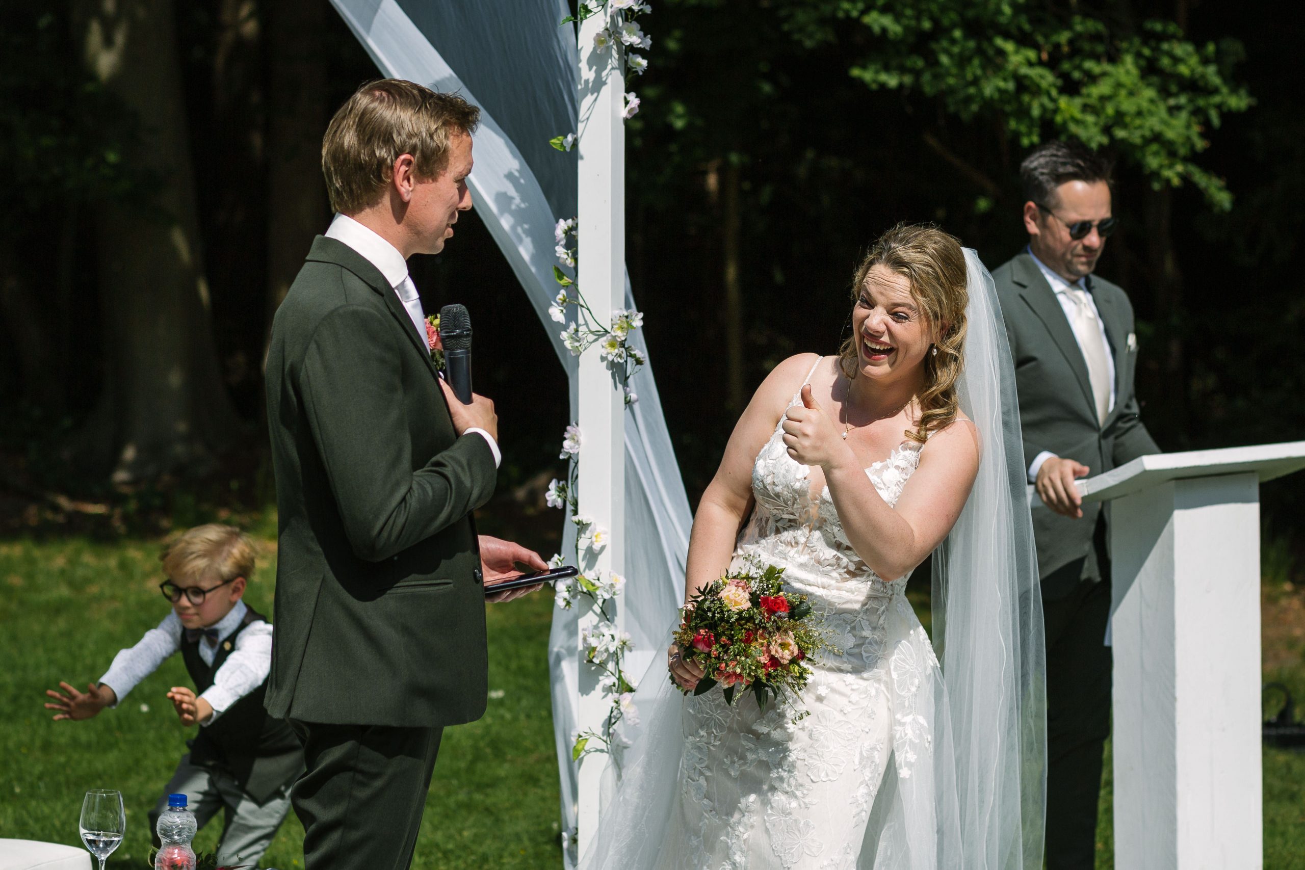 bride giving the thumbs up during the outdoor wedding ceremony natural unposed candid wedding photography by LGBTQ_friendly documentary wedding photographer surrey sussex
