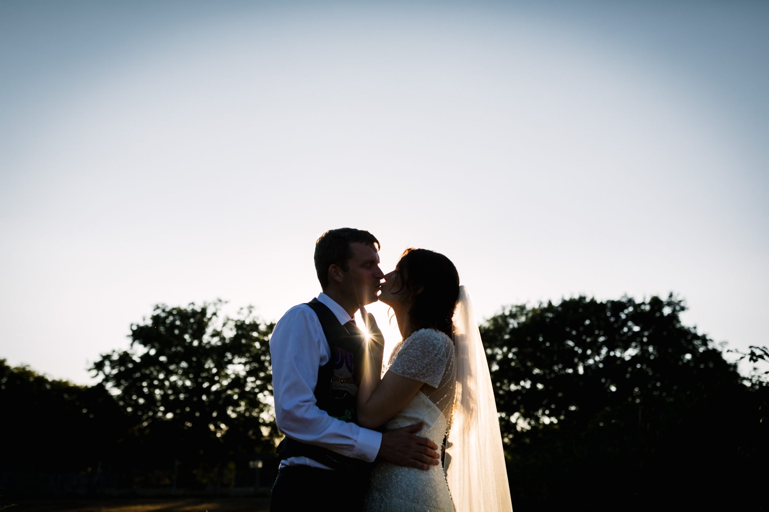 bride and groom portrait sharing a kiss during golden hour sunburst natural unposed candid wedding photography by LGBTQ_friendly documentary wedding photographer surrey sussex