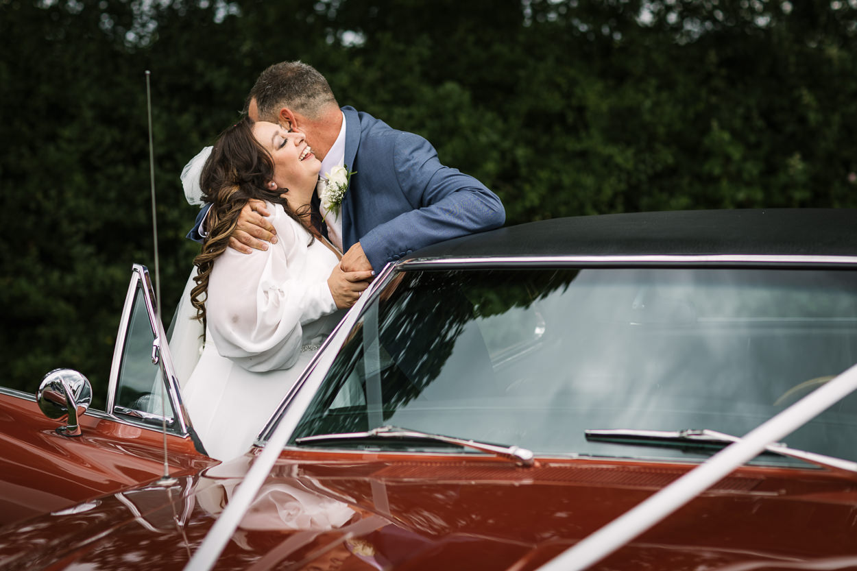 bride and groom loving embrace during outdoor portraits with wedding cars at  gildings_barns wedding photography by documentary wedding photographer surrey sussex