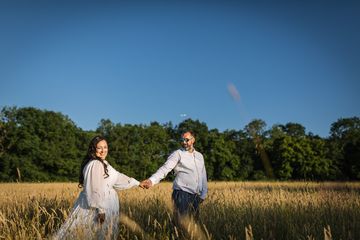 bride and groom looking at photographer outdoor portraits golden_hour in field with tall grass walking hand in hand at relaxed gildings_barns wedding photography by documentary wedding photographer surrey sussex