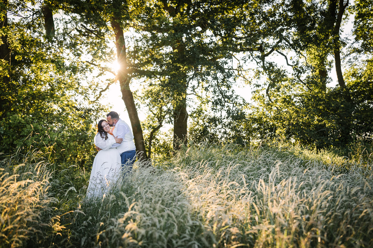 bride and groom outdoor portraits golden_hour posing in front of trees with sunlight shining through from behind at relaxed gildings_barns wedding photography by documentary wedding photographer surrey sussex