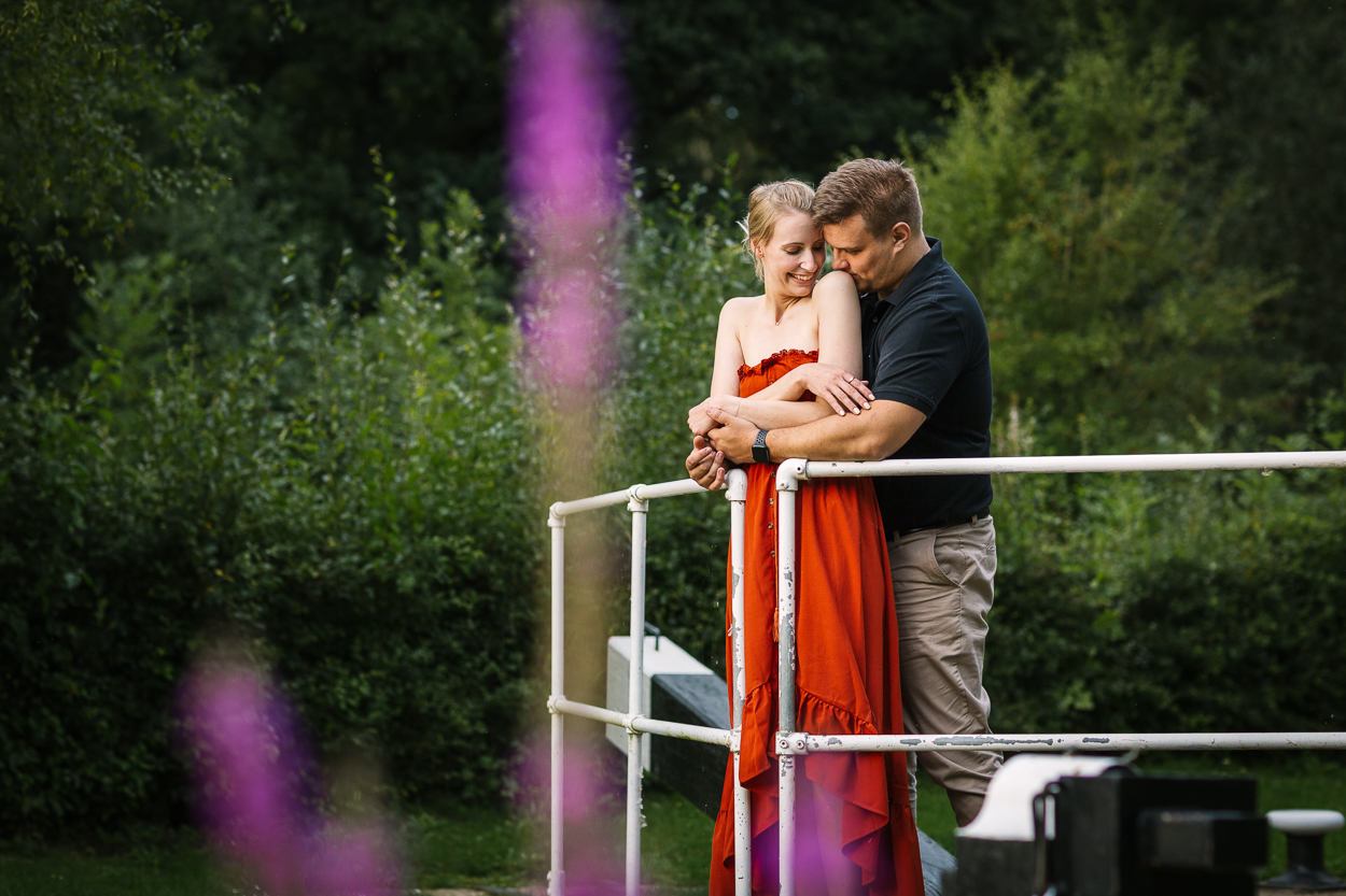 couple hugging on bridge over water, purple flower in foreground candid engagement_shoot relaxed Pre_wedding_shoot sussex surrey by documentary wedding photographer