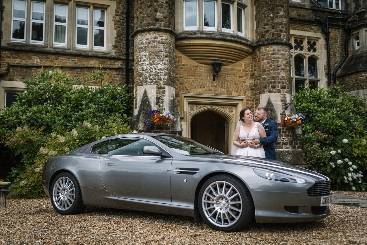 bride and groom portrait with aston_martin wedding car outside at Hartsfield_Manor_wedding Surrey by documentary wedding photographer surrey for candid natural unposed authentic documentary photography