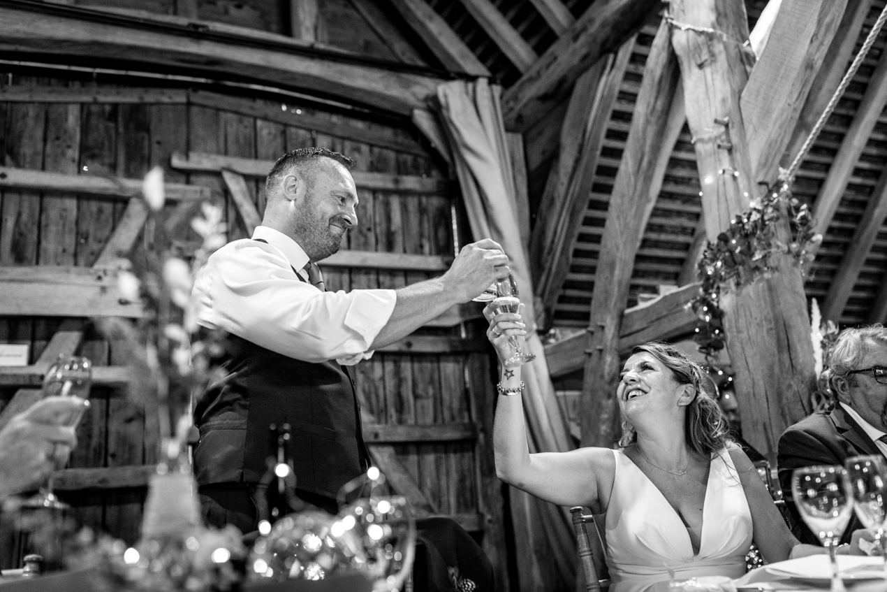 black_white image of bride and groom toasting during wedding breakfast candid gildings_barns wedding photography by documentary wedding photographer surrey sussex
