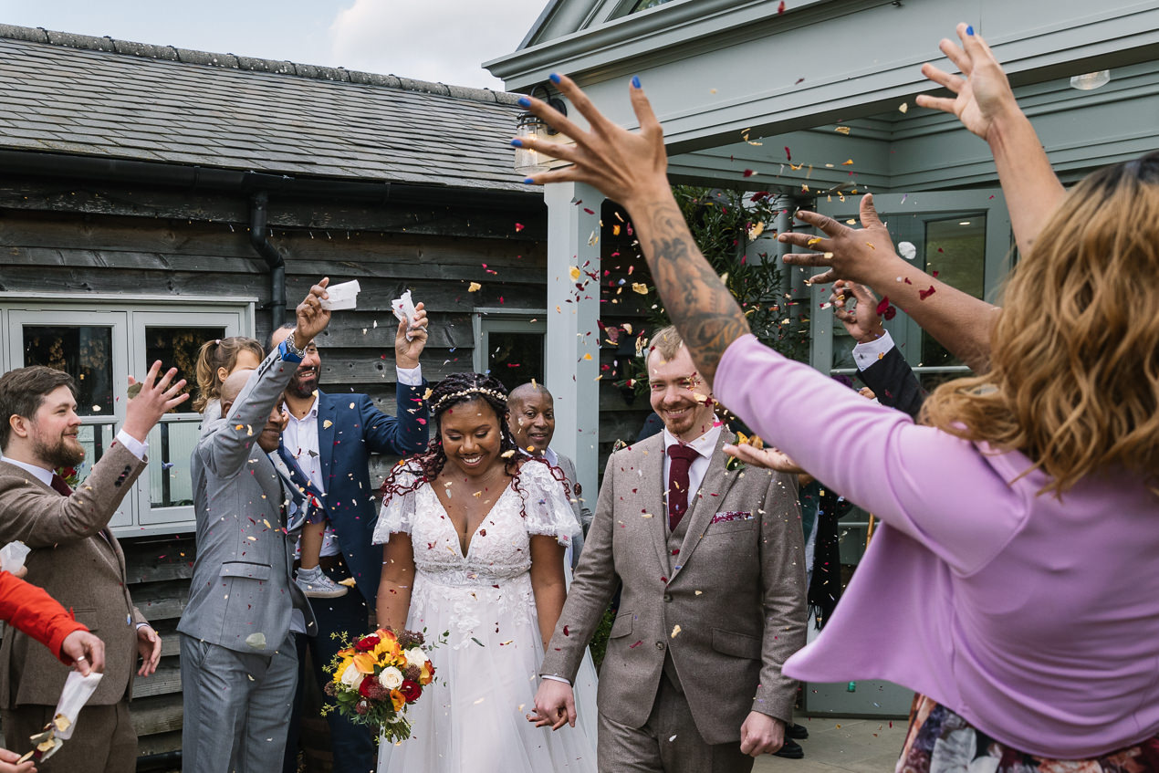 confetti exit of bride and groom after ceremony at relaxed gate_street_barn wedding guildford with candid unposed natural storytelling wedding photography by documentary wedding photographer surrey sussex